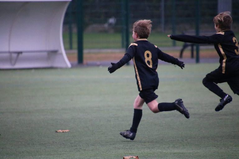 Deux jeunes joueurs de football en maillot noir courant sur le terrain lors d’un match de la catégorie U11 à U13.